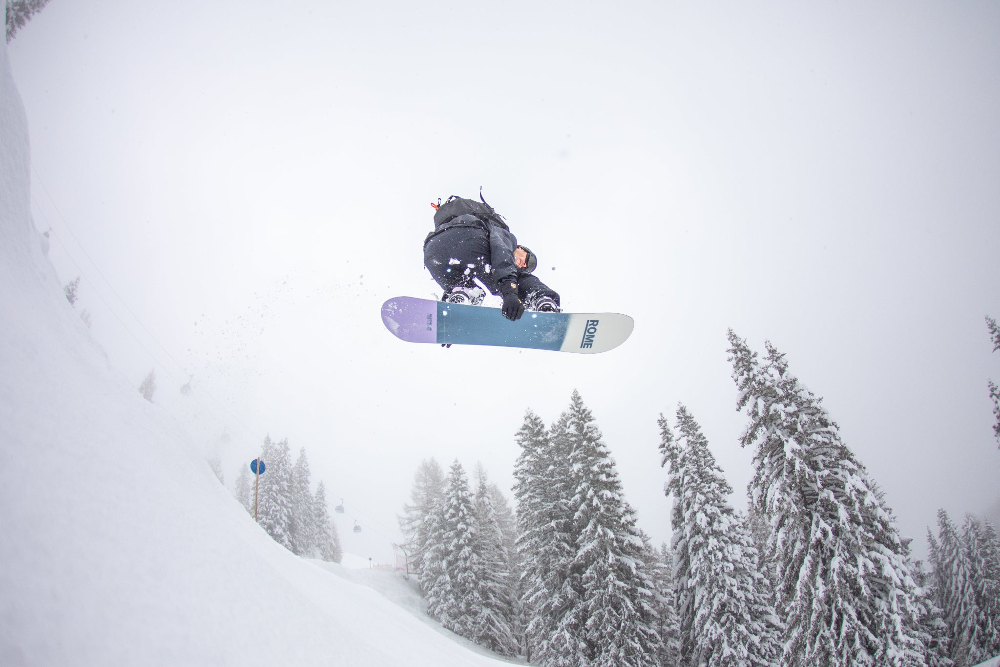 Person snowboarding in the air with a snowy landscape and trees in the background