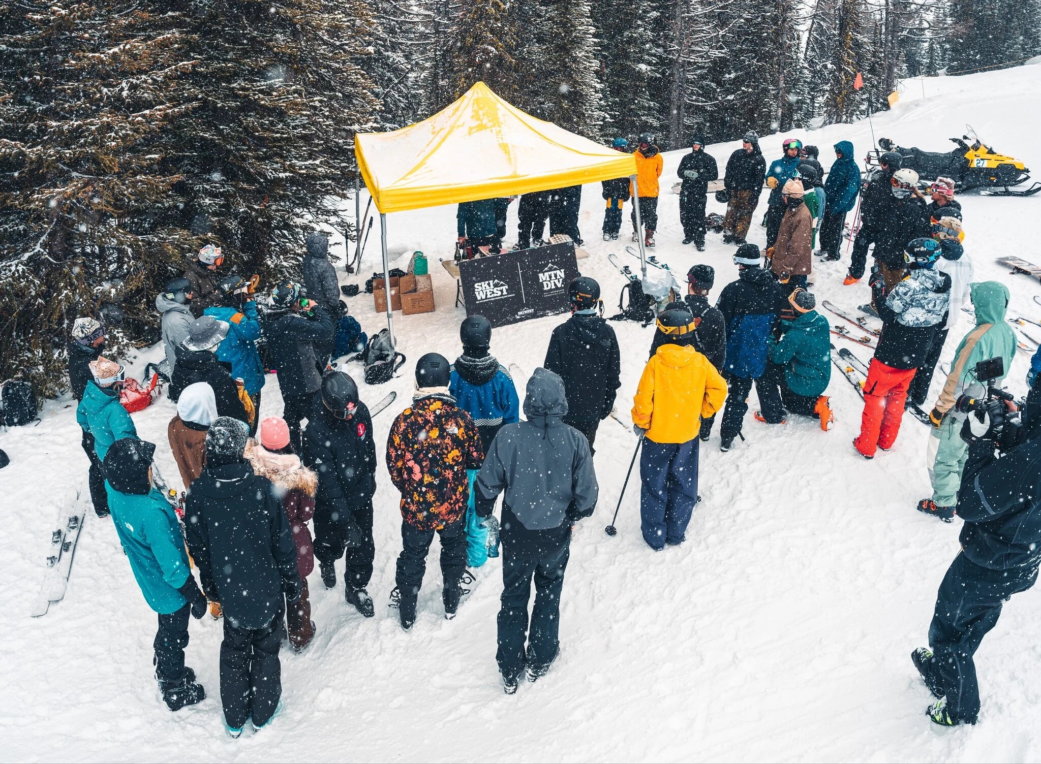Group of people gathered around a yellow tent in a snowy outdoor setting